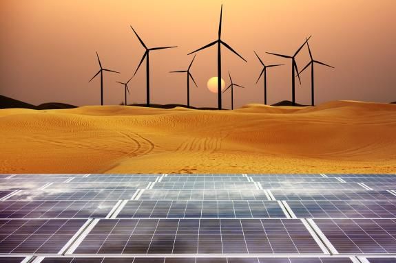 Renewable energy with windmills and solar panels in desert at sunset