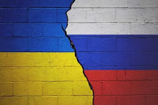 Cracked brick wall painted with a Ukrainian flag on the left and a Russian flag on the right.