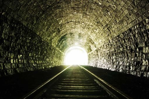 Rail tracks running through a tunnel with a light at the end of it.