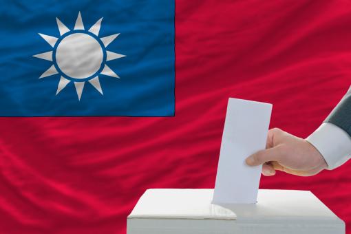 Man putting ballot in a box during elections in Taiwan in front of flag