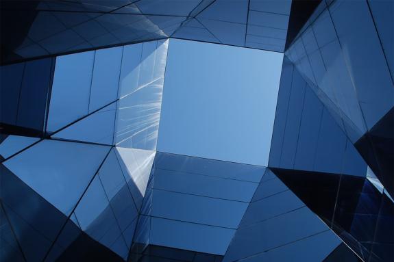 Reflective blue glass panels forming geometric shapes against a clear blue sky.
