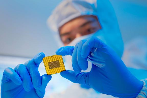 Male design engineer in sterile coverall holds microchip with gloves and examines it - ultra modern electronic manufacturing factory